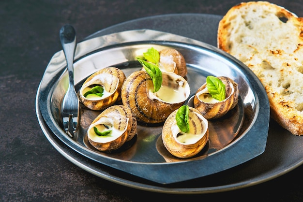 Caracoles de Borgoña con salsa de mantequilla de hierbas de ajo y pan en una sartén de aluminio sobre fondo oscuro