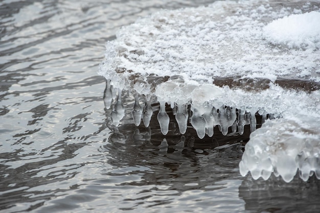 Los carámbanos cuelgan bajo el hielo contra el fondo de un río caído en primavera Grandes piedras cubiertas de carámbanos