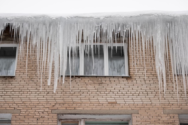 Foto los carámbanos grandes que cuelgan del techo cubierto de nieve de una casa de ladrillos indican un mal aislamiento del techo