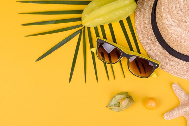 Carambol de frutas, accesorios de playa y follaje de una planta tropical sobre papel de colores. Fondo de verano con estrellas de mar y frutas.