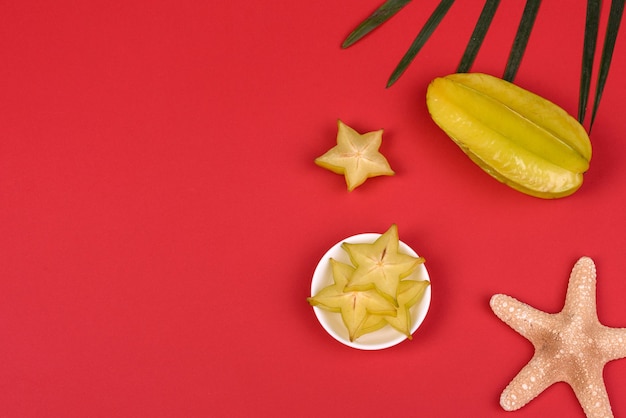 Carambola de frutas, acessórios de praia e folhagem de planta tropical em papel colorido. Fundo de verão com estrelas do mar e frutas