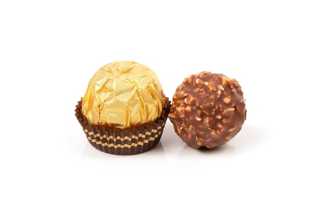 Un caramelo redondo en un paquete dorado y un caramelo sin envolver vertido con migas de chocolate y gofres