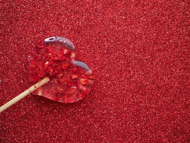 Un caramelo rojo en forma de corazón con un palo de madera sobre un fondo rojo.