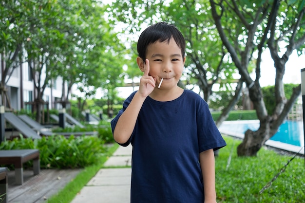 Caramelo y sonrisa del vago del muchacho lindo asiático Sostenga dos dedos en el fondo de la naturaleza verde