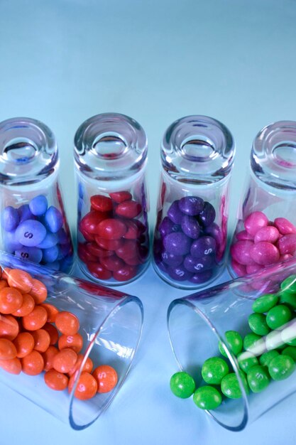 Caramelos brillantes multicolores en vasos transparentes sobre un fondo azul Vasos de arco iris