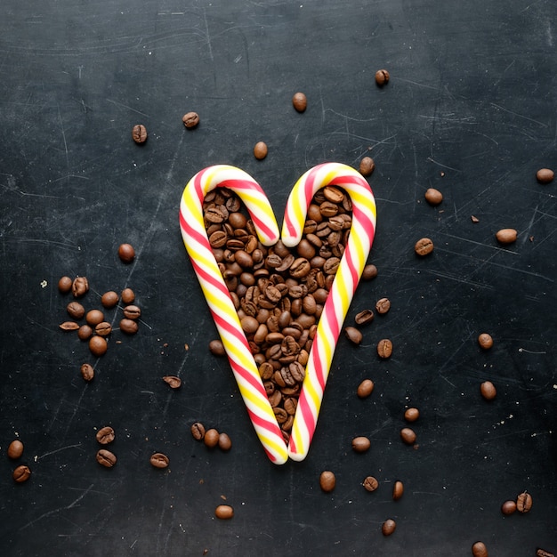 Caramelos de caña en forma de corazón con granos de café vista plana sobre fondo negro