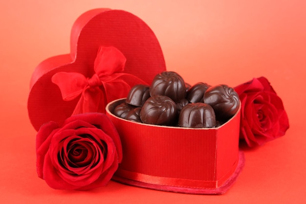 Caramelos de chocolate en caja de regalo, sobre fondo rojo.