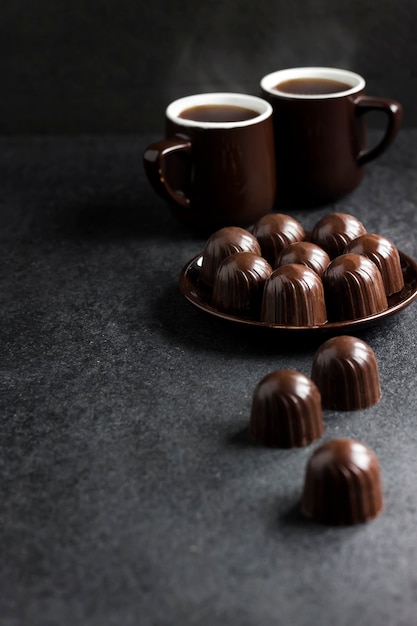 Caramelos de chocolate en un plato y dos tazas de café caliente sobre fondo negro con espacio de copia