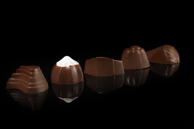 Caramelos de chocolate sobre una superficie oscura con reflejo. Relleno de frutos secos y frutas. Copie el espacio.