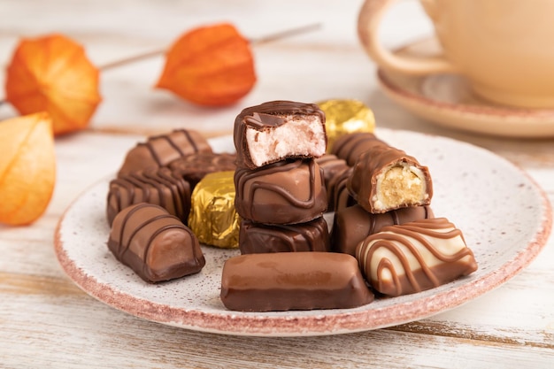 Caramelos de chocolate con taza de café y flores de physalis sobre un fondo blanco de madera vista lateral enfoque selectivo