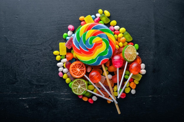 Caramelos de colores, dulces y piruletas. Sobre un fondo de madera negra. Vista superior. Espacio libre.