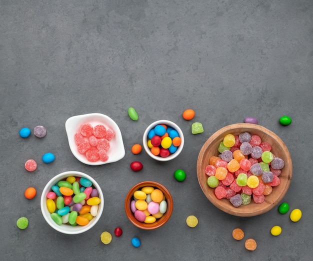 Caramelos de colores surtidos en tazones sobre fondo de piedra con espacio de copia