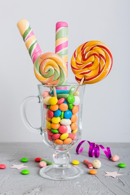 Caramelos coloridos en taza en la mesa sobre un fondo claro Granos piruletas giratorias Concepto creativo de un frasco lleno de deliciosos dulces de la tienda de caramelos