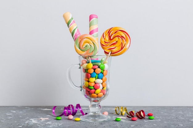 Caramelos coloridos en taza en la mesa sobre un fondo claro Granos piruletas giratorias Concepto creativo de un frasco lleno de deliciosos dulces de la tienda de caramelos