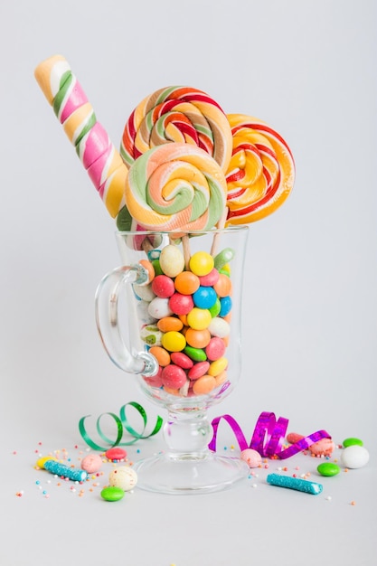 Caramelos coloridos en taza en la mesa sobre un fondo claro Granos piruletas giratorias Concepto creativo de un frasco lleno de deliciosos dulces de la tienda de caramelos