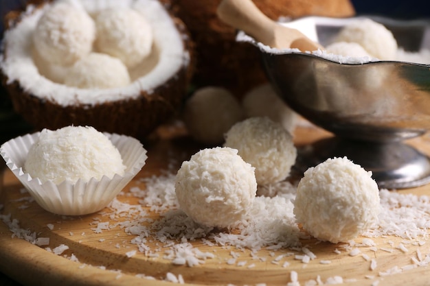 Caramelos en copos de coco y coco fresco en tablero de madera, primer plano