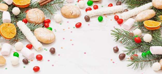 Caramelos y galletas con ramas de árboles de Navidad sobre fondo de mármol blanco