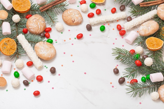 Caramelos y galletas con ramas de árboles de Navidad sobre fondo de mármol blanco