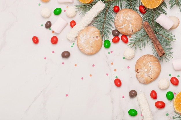 Caramelos y galletas con ramas de árboles de Navidad sobre fondo de mármol blanco