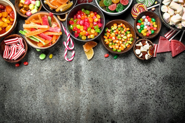 Caramelos multicolores, gelatina y malvaviscos en un bol. Sobre una mesa rústica.