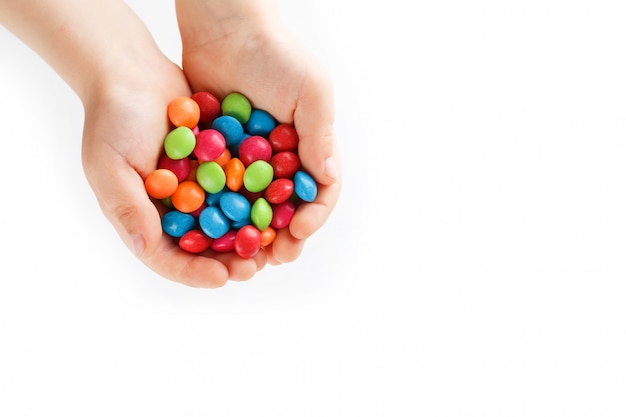 Caramelos multicolores en manos de un niño sobre un fondo blanco.