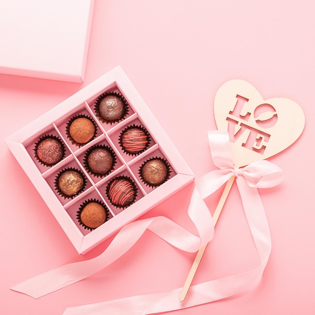 Caramelos de trufa de chocolate y corazón de madera con texto amor fondo rosa Regalos comida festiva concepto de amor Marco cuadrado