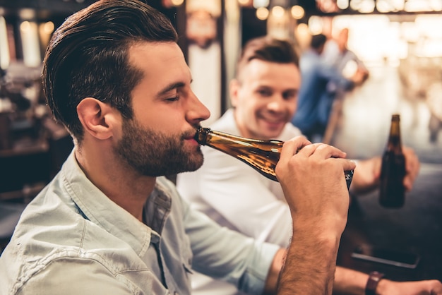 Caras bonitos estão bebendo cerveja no bar.