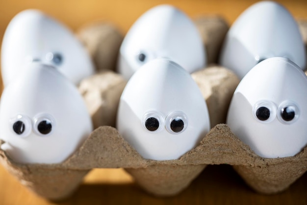 Caras divertidas en huevos blancos en caja de cartón con huevos de pollo orgánicos en la mesa de la cocina primer plano grandes ojos de animación humor comida y concepto de vacaciones de Pascua