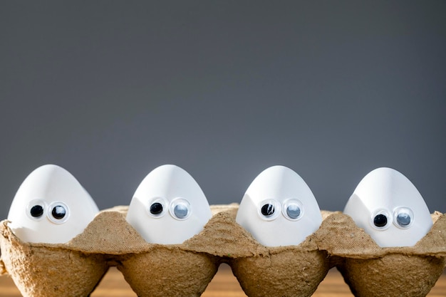 Caras divertidas en huevos blancos en caja de cartón con huevos de pollo orgánicos en la mesa de la cocina primer plano grandes ojos de animación humor comida y concepto de vacaciones de Pascua