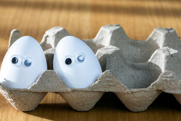 Caras engraçadas em ovos brancos em caixa de papelão com ovos de galinha orgânicos na mesa da cozinha closeup grande animação olhos humor comida e conceito de feriado de páscoa