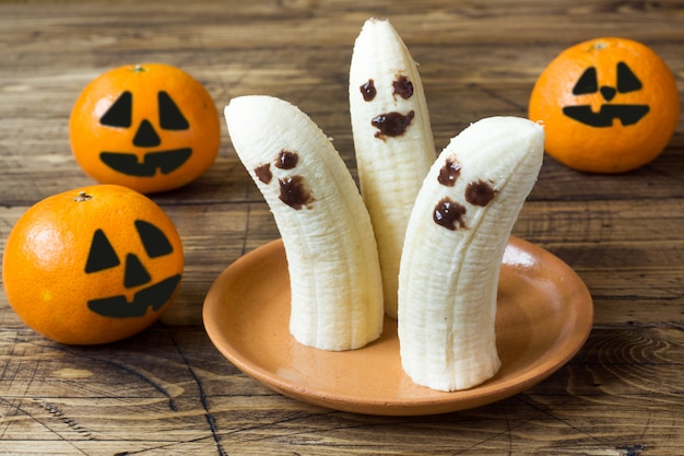 Caras engraçadas pintadas em tangerinas e bananas para o halloween