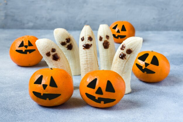 Caras engraçadas pintadas em tangerinas e bananas para o Halloween