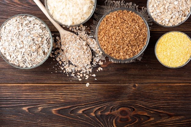 Carbohidratos. Varios copos de grano en cuencos sobre mesa de madera oscura.