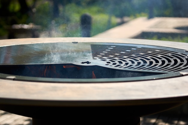 Carbón llameante en el hoyo de la parrilla del hervidor con rejilla de hierro fundido. Superficie de cocción de mesa redonda. Parrilla caliente para barbacoa con rejilla de acero inoxidable en el patio trasero para asar alimentos al aire libre. Ase con llamas adentro.