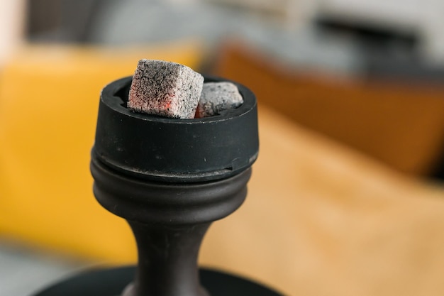 Carbón de narguile para fumar en primer plano y ocio con iluminación natural en la habitación