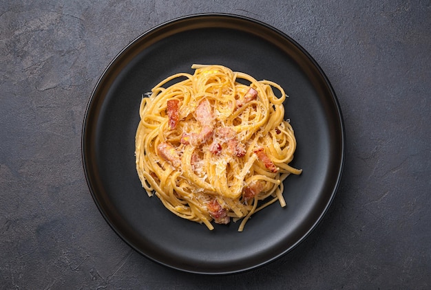 Carbonara de pasta italiana tradicional con tocino parmesano huevo y pimienta sobre un fondo oscuro Vista superior