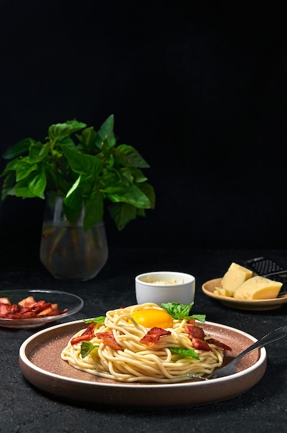 Carbonara de pasta italiana tradicional con tocino, queso y yema de huevo en la placa sobre fondo oscuro