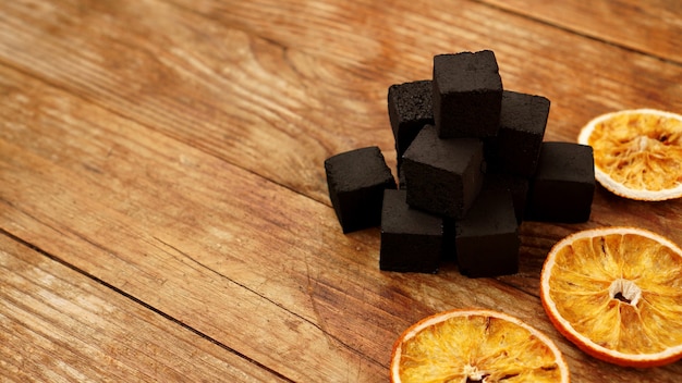 Carbones para narguile sobre fondo de madera con naranjas secas. Lugar para el texto