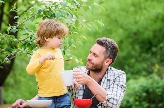 Cardápio para crianças. Família desfrutar de refeição caseira. Hábitos alimentares. Garotinho com pai comendo fundo de natureza de quintal de piquenique de comida. Café da manhã de verão. Conceito de comida saudável. Pai filho come comida e se diverte.