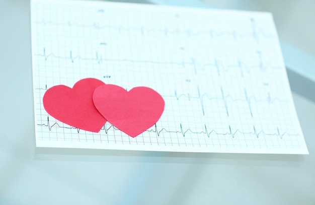 Foto cardiograma y dos corazones de papel rojo sobre la mesa