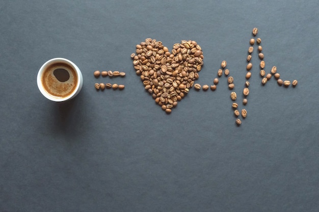 Un cardiograma de granos de café y una taza de café sobre una mesa negra.