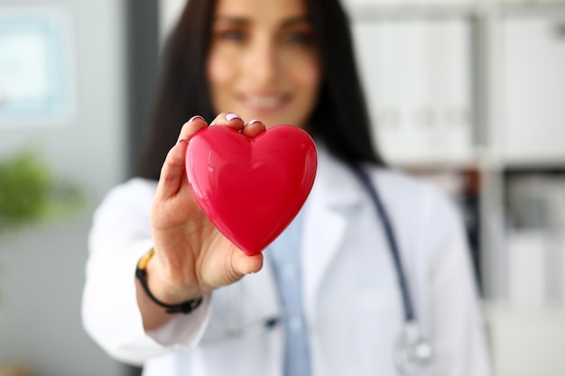 Foto cardiologista feminino segurando nos braços coração de brinquedo vermelho