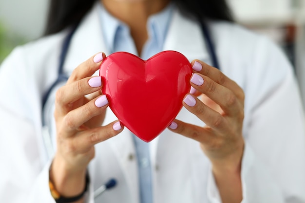 Cardiólogo femenino sosteniendo en brazos corazón de juguete rojo