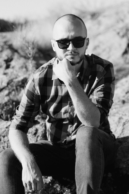 Careca com barba usando uma camisa jeans e tênis de trekking em pedras de granito