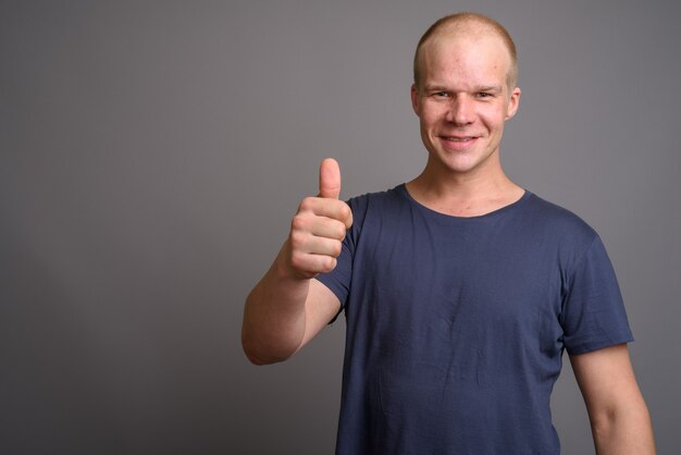 Careca com camisa azul encostada na parede cinza