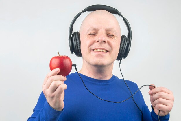 careca com fones de ouvido ouve música através de um jogador de maçã vermelha. Metáfora e conceito de benefícios vitamínicos em música e som