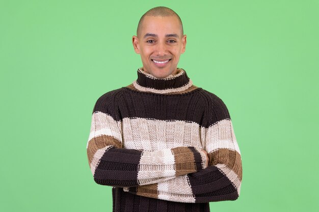 Careca e bonito homem multiétnico pronto para o inverno contra uma parede verde