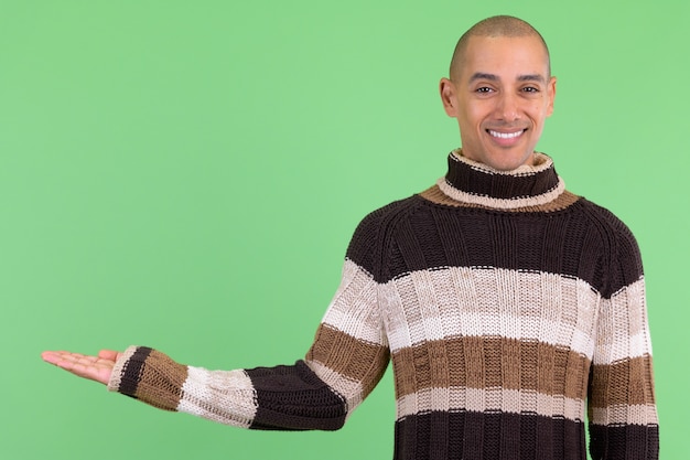 Careca e bonito homem multiétnico pronto para o inverno contra uma parede verde