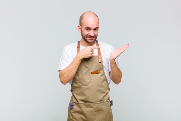 Careca sorrindo alegremente e apontando para copiar espaço na palma da mão ao lado, mostrando ou anunciando um objeto