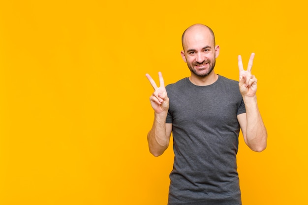 Careca sorrindo e parecendo feliz, amigável e satisfeito, gesticulando vitória ou paz com as duas mãos